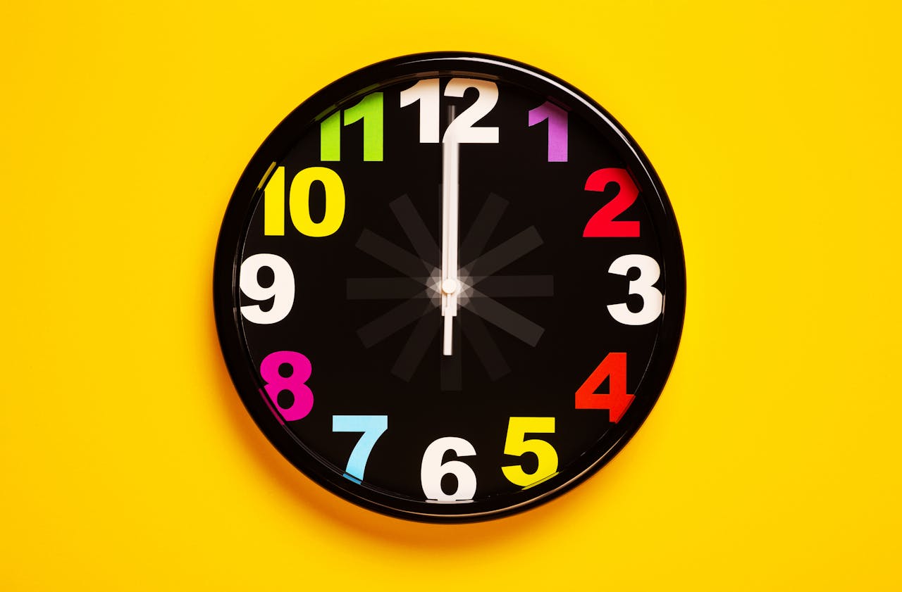 about-us-02 Vibrant wall clock with colorful numbers on a bright yellow background, emphasizing modern decor.