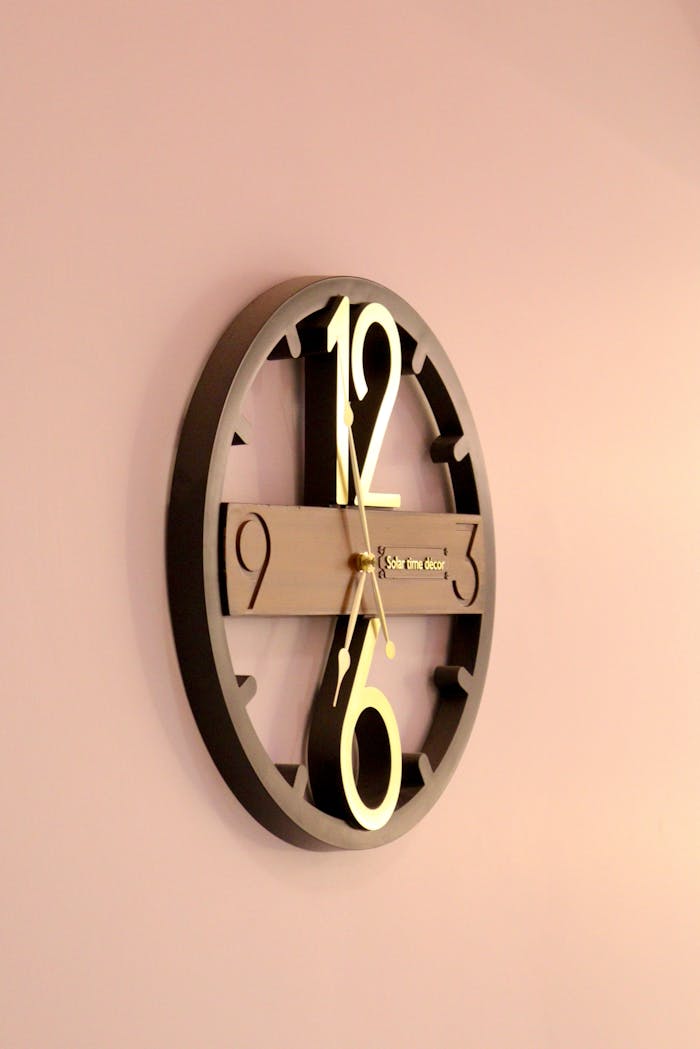about-us-01 Stylish round wall clock with gold accents against a pastel pink background.